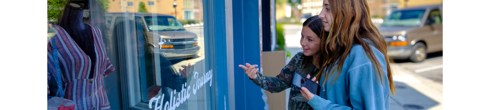 Two teenage girls admire a dress in a boutique window, excited to pay using their debit card stored in a digital wallet.